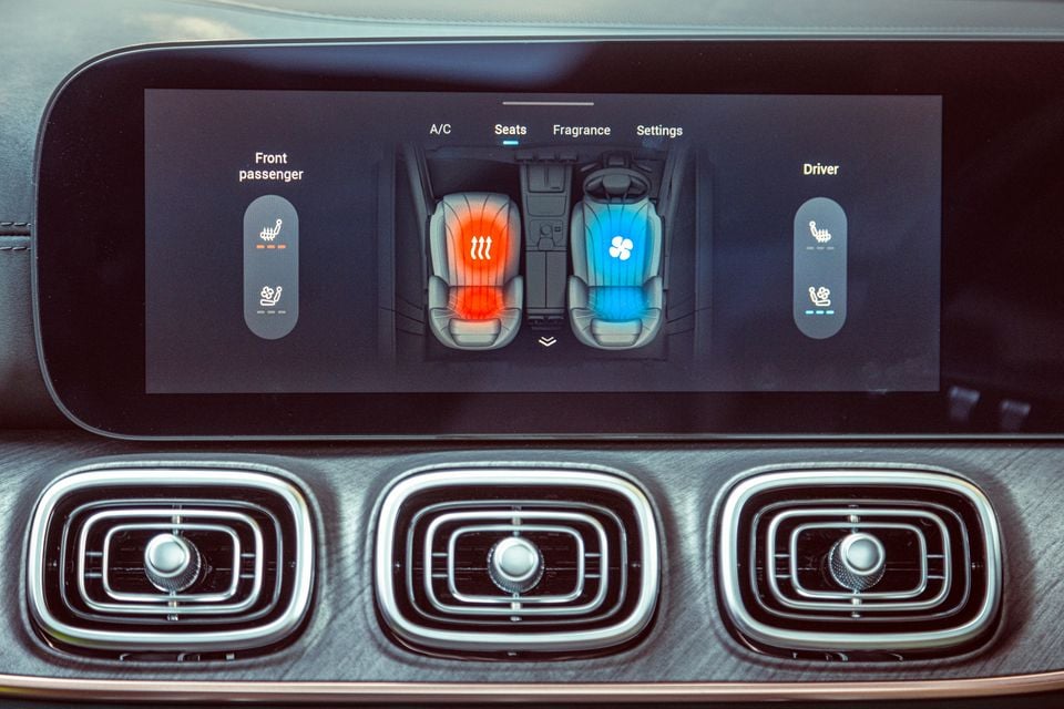 A car infotainment screen showing the seat heating and ventilation controls, with the front passenger seat set to heated (red) and the driver seat set to ventilated (blue), above three air vents on the centre console.