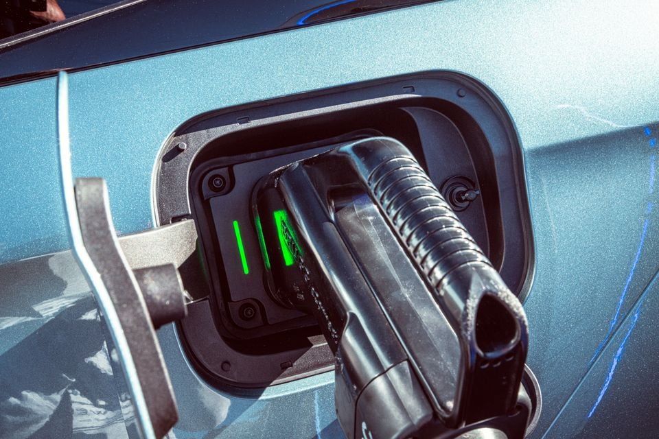 A charging plug connected to the charging port of a blue electric or plug-in hybrid vehicle, with green indicator lights visible