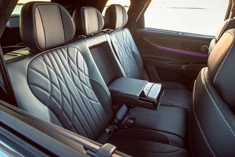 The rear interior of a Jaecoo J8 showing black leather seats with diamond-stitch detailing, a fold-down centre armrest, and ambient purple lighting along the door trim.