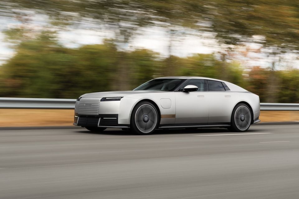 A silver Jaguar Type 00 concept sedan driving on a highway, seen from the side.