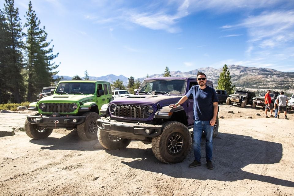 A purple Jeep Wrangler 392 and a green Jeep Wrangler Rubicon on the Rubicon Trail, with a man in sunglasses leaning on the purple Jeep