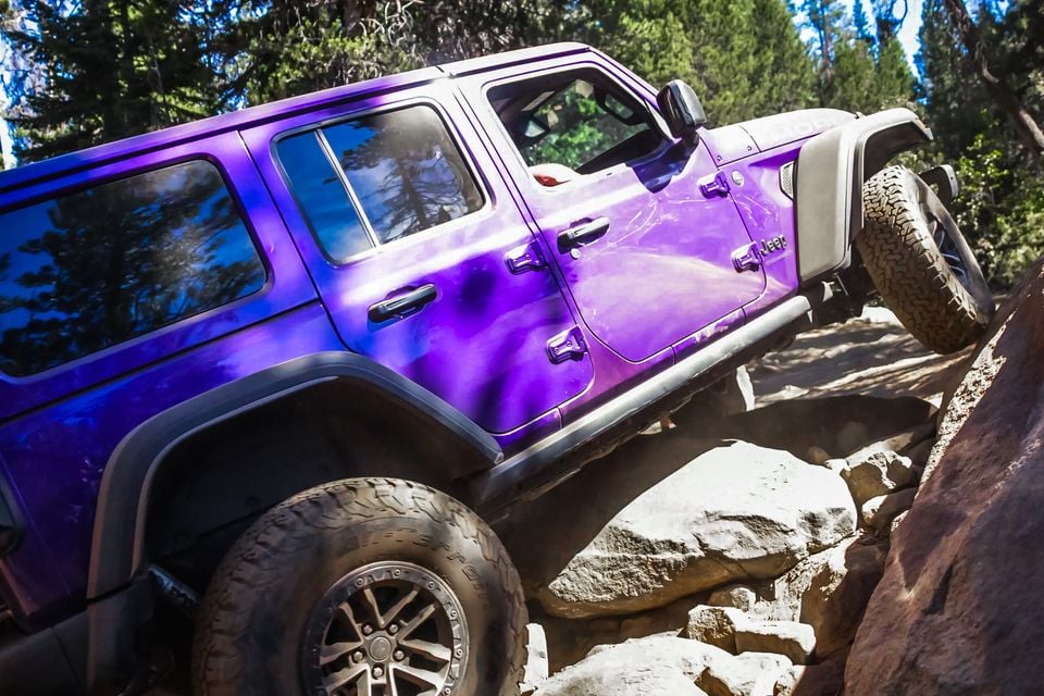 A purple Jeep Wrangler 392 four-door seen from the side as it climbs over large boulders on the Rubicon Trail