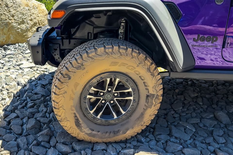 Close-up of the front wheel of a purple Jeep Wrangler 392 with a muddy BFGoodrich All-Terrain tyre and beadlock-style alloy, parked on rocks