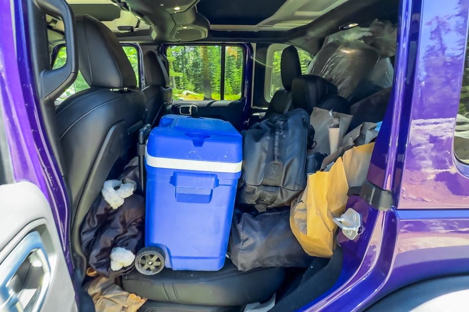Rear seat of a purple Jeep Wrangler 392 packed with a blue wheeled cooler, bags and camping gear, seen through the open rear door