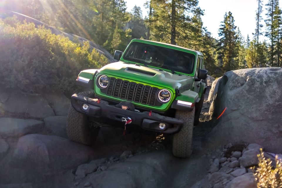 A green Jeep Wrangler Rubicon 392 crawling over large granite boulders on the Rubicon Trail, surrounded by pine trees