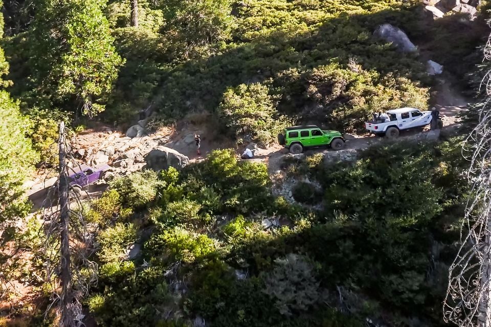 Aerial view of a green Jeep Wrangler, a white Jeep Gladiator and a purple Jeep Wrangler on a rocky forest trail on the Rubicon Trail