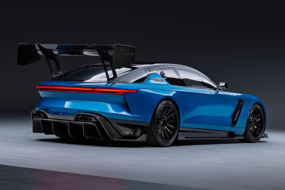 A blue Jensen Interceptor GTX prototype sports car seen from the rear three-quarter angle, featuring a large rear wing, carbon fibre diffuser, and full-length tail-lights, displayed in a studio setting.