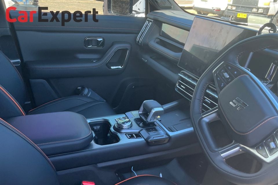 Interior of a Jetour SUV showing the black leather front seats with orange stitching, centre console with gear selector, large touchscreen and steering wheel