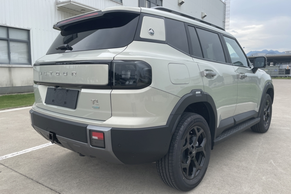A light grey Jetour T1 PHEV SUV parked outside a building, seen from the rear passenger side with black wheels and a tailgate spoiler