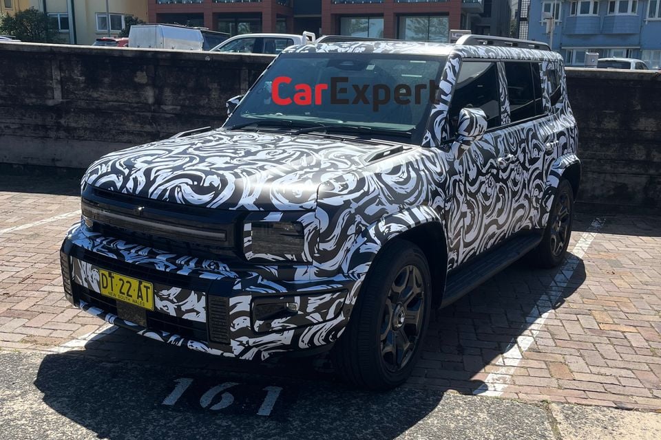A camouflaged Jetour T2 SUV prototype with swirling black and white wrap and NSW number plates, parked in a brick-paved car park