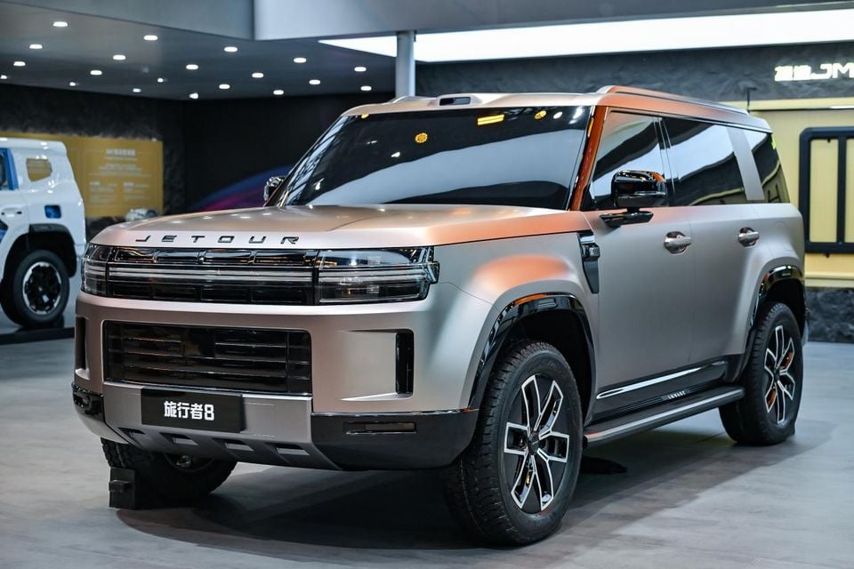A Jetour T8 SUV displayed at a motor show, seen from the front-side angle in a silver and bronze two-tone finish