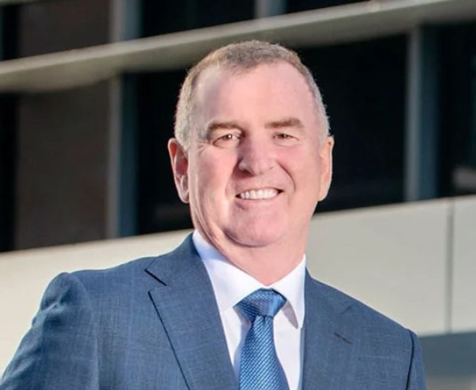 A man in a blue suit and tie smiling in front of a modern building, identified as GWM chief operating officer John Kett