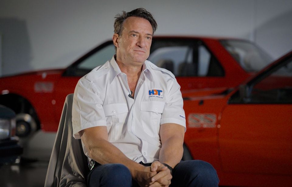 HDT Special Vehicles' Kenny Habul seated in an HDT shirt in front of red Holden Commodore SS performance cars