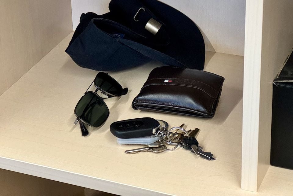 A car key fob with keys, a leather wallet, sunglasses, and a cap on a shelf