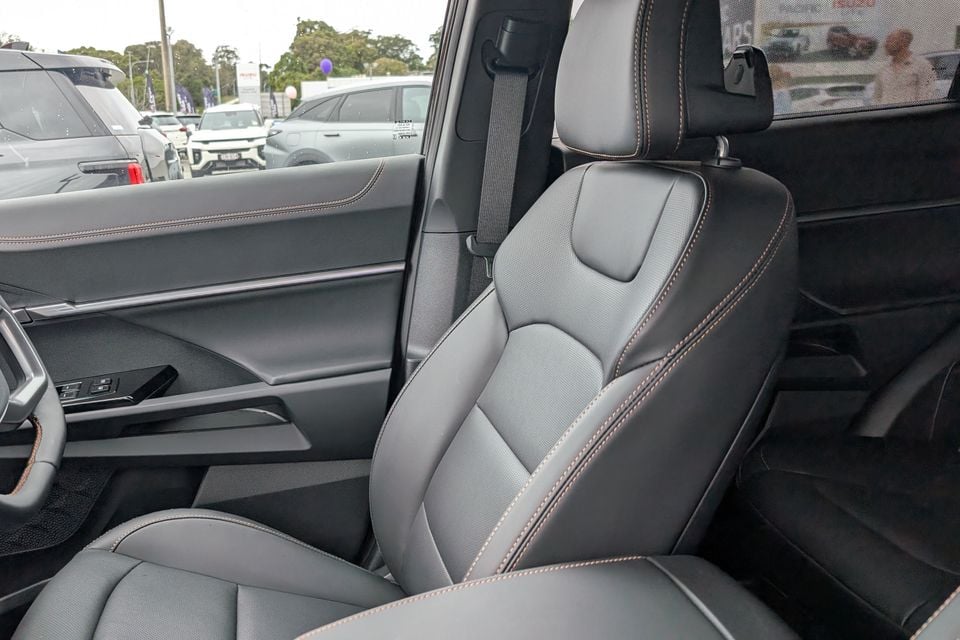 Interior view of a KGM Torres EVX showing the front passenger seat with dark leather upholstery and contrasting stitching, viewed from the rear door opening at a dealership