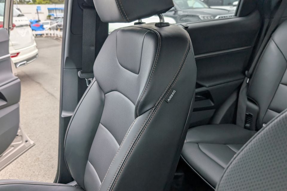 Black leather car seat with contrast stitching and an airbag label visible on the side bolster, with rear seating visible behind