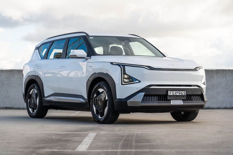 A white Kia EV5 electric SUV seen from the front-side angle in an open car park