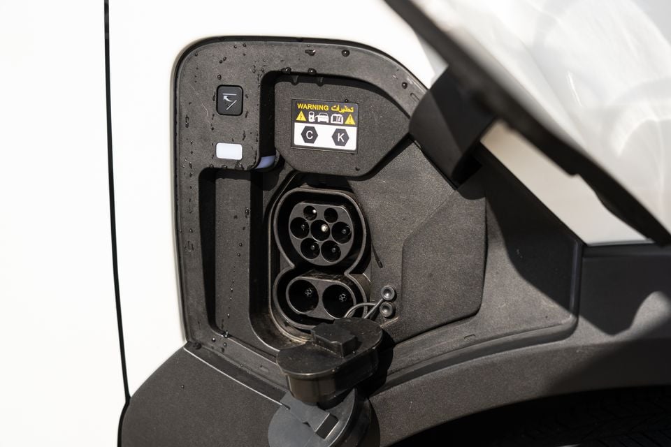 Close-up of the CCS charging port on a white Kia EV5, with the charge flap open showing Type 2 AC and DC fast-charge inlets and a warning label