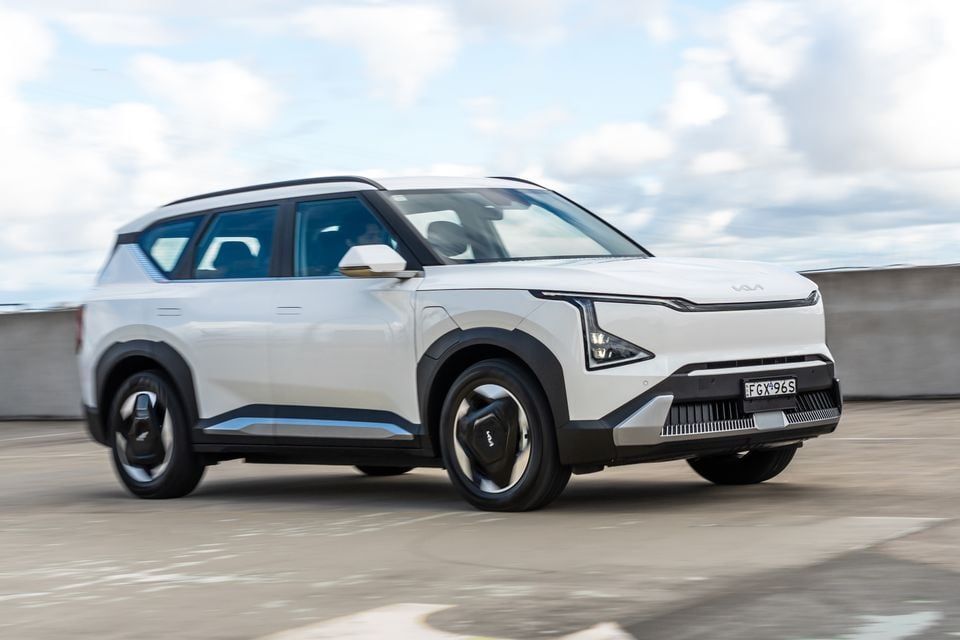 A white Kia EV5 electric SUV seen from the front-side angle, driving on a rooftop car park