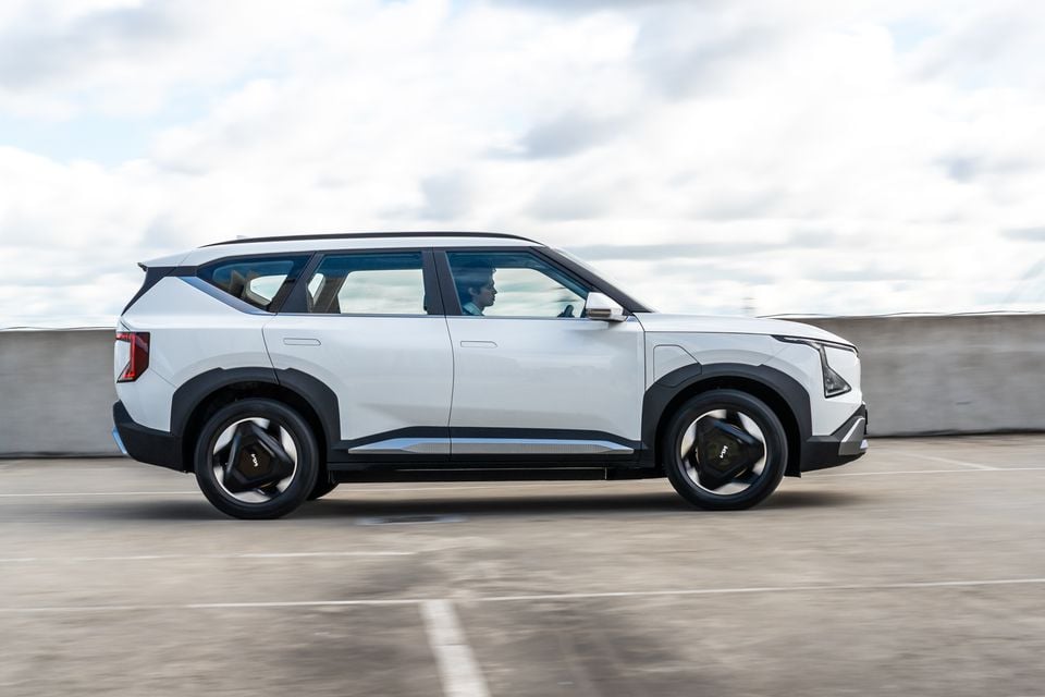 A white Kia EV5 SUV seen from the side while driving through a car park