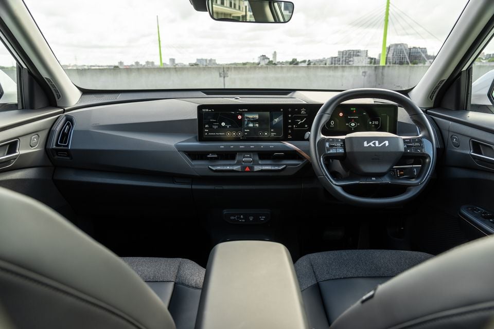 Kia EV5 interior showing the wide dual-screen infotainment and instrument display, steering wheel with Kia logo, and front seats