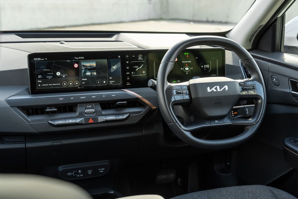 Kia EV5 interior showing the dual widescreen display, steering wheel with Kia logo, and dashboard controls from the driver's perspective