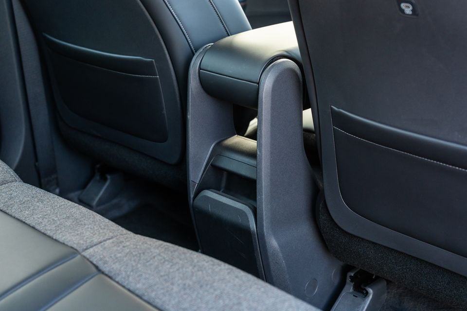 Car interior showing the centre console area between the front seats, with dark leather upholstery and a rear armrest, viewed from the rear passenger area of a Kia EV5