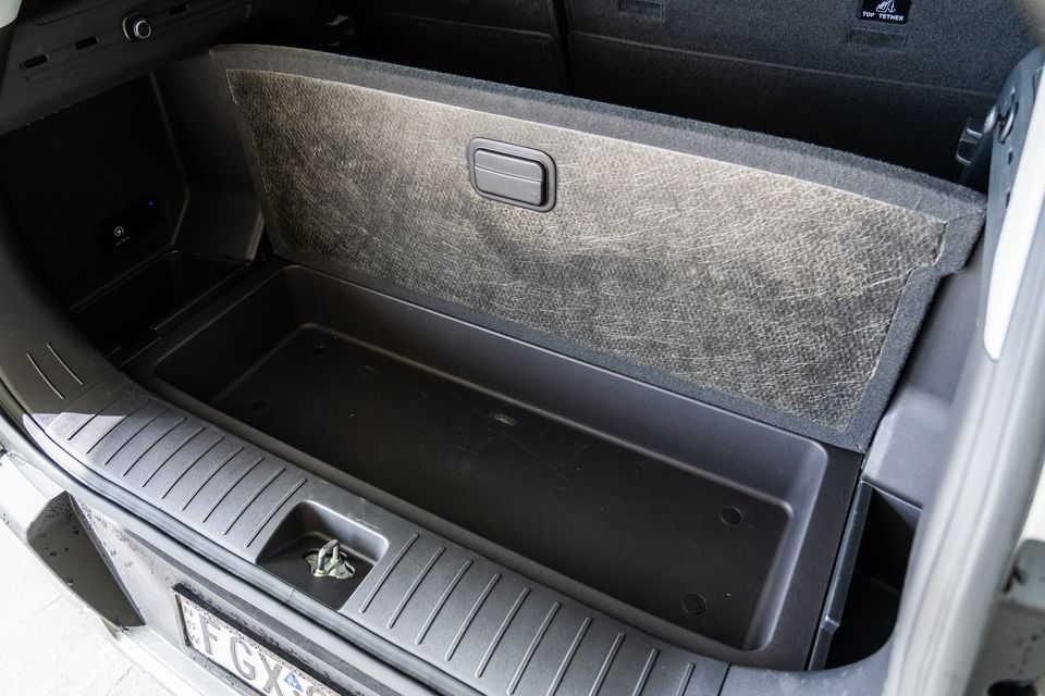 The boot of a Kia EV5 SUV open, showing a carpeted cargo floor with a under-floor storage tray and a top tether anchor point visible on the rear seatback