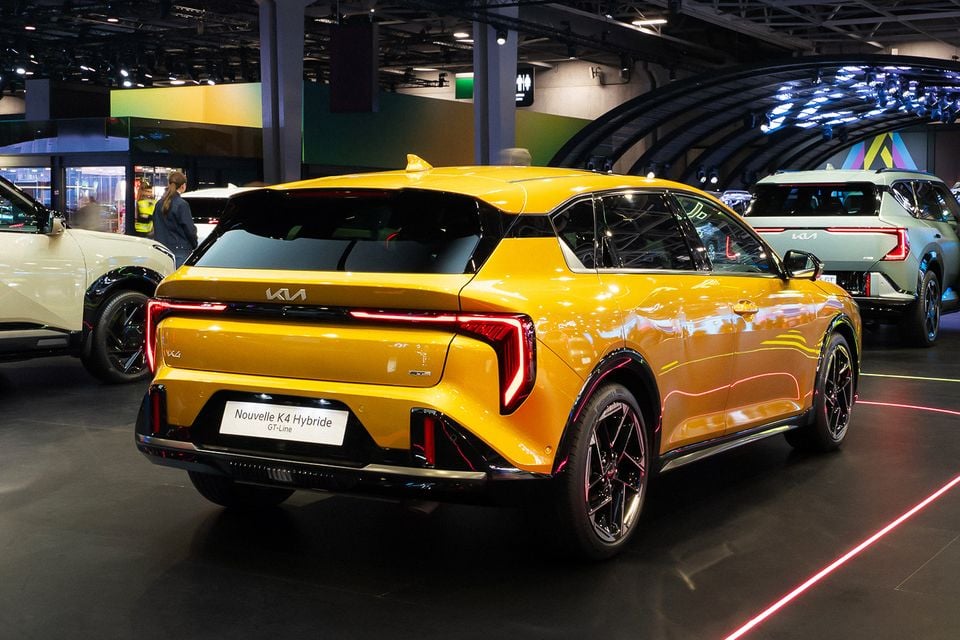 A yellow Kia K4 Hybrid GT-Line hatch seen from the rear on display at the Paris Motor Show, with other Kia models nearby