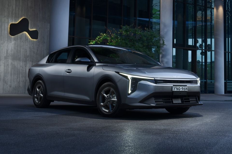 A silver Kia K4 S sedan seen from the front-side angle, parked outside a modern building at dusk