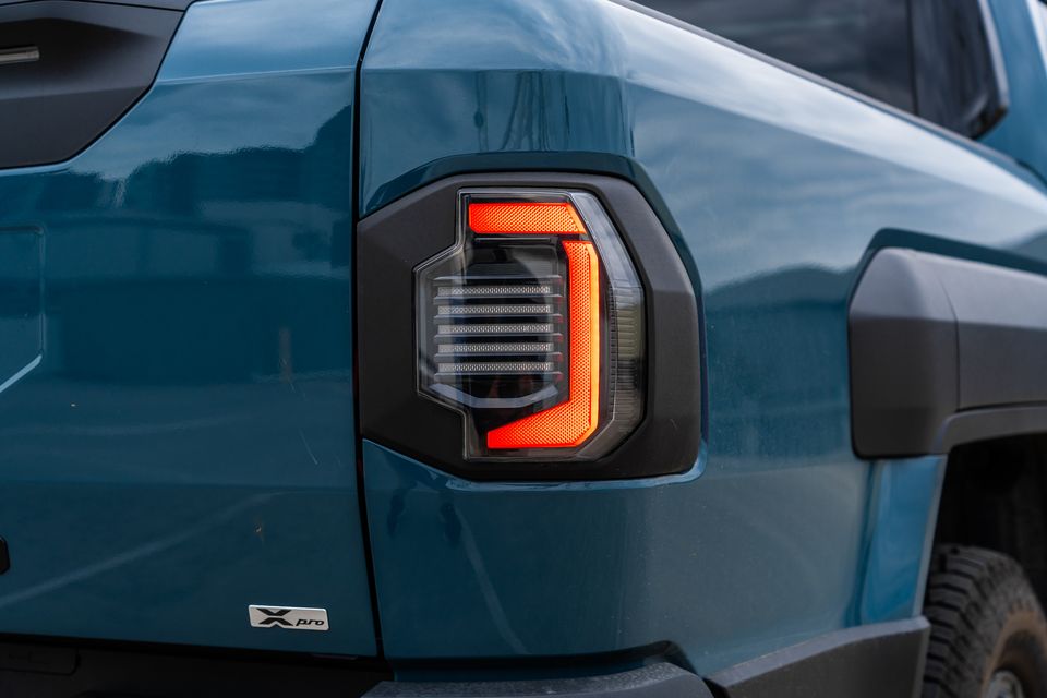 Close-up of the tail light on a blue Kia Tasman X Pro ute, showing an illuminated LED tail light with a distinctive red surround and X Pro badge visible on the rear quarter panel.