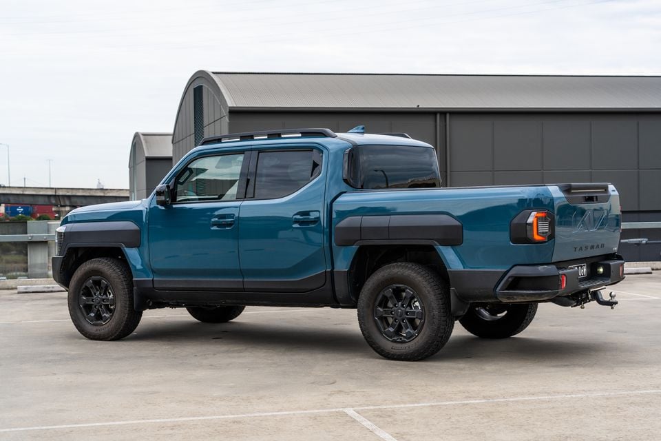 A blue Kia Tasman dual-cab ute seen from the rear three-quarter angle in a car park