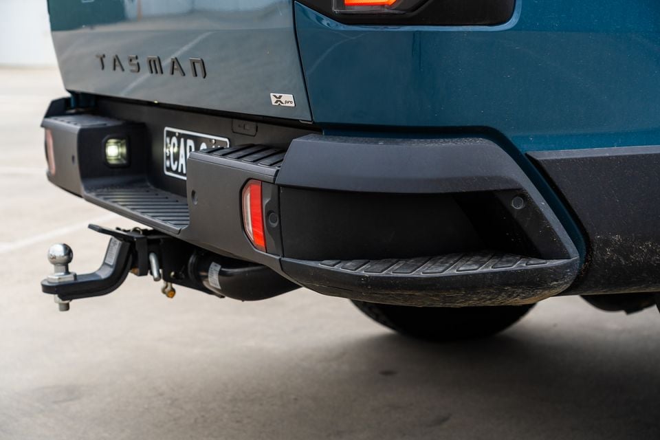 Close-up of the rear bumper of a Kia Tasman X Pro ute, showing the tow ball hitch, step, rear reflectors and tailgate badging