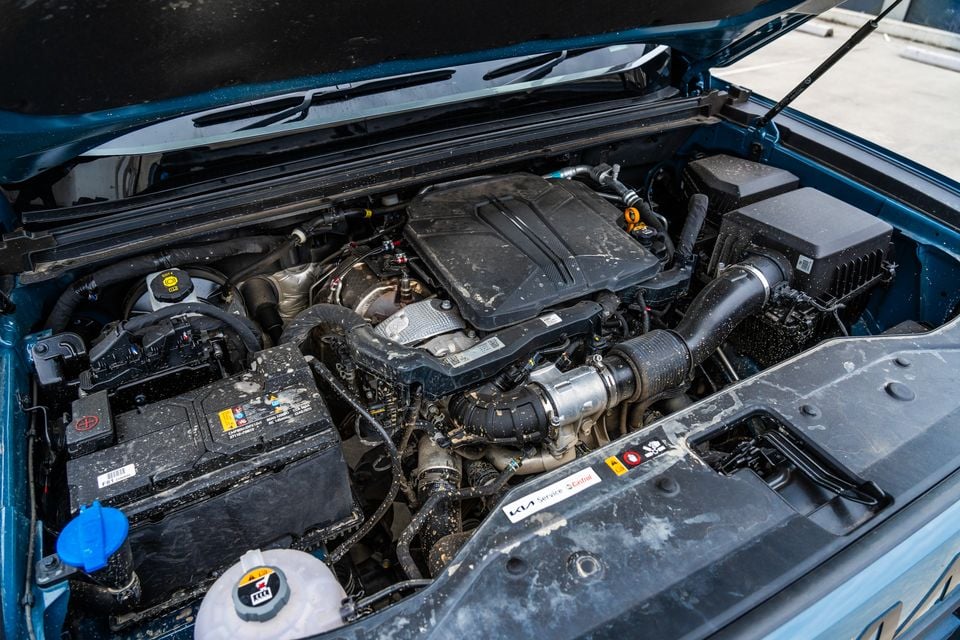 Engine bay of a Kia Tasman X-Pro with the bonnet open, showing a turbocharged engine covered in dirt and grime