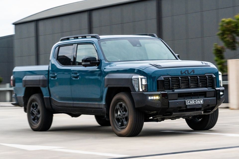 A blue Kia Tasman dual-cab ute seen from the front-side angle in a car park