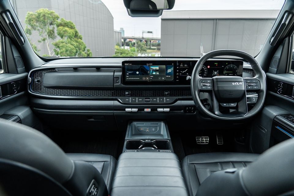 Interior of a Kia Tasman X-Pro showing the dashboard, dual infotainment and instrument display screens, steering wheel, centre console and front seats in right-hand drive configuration