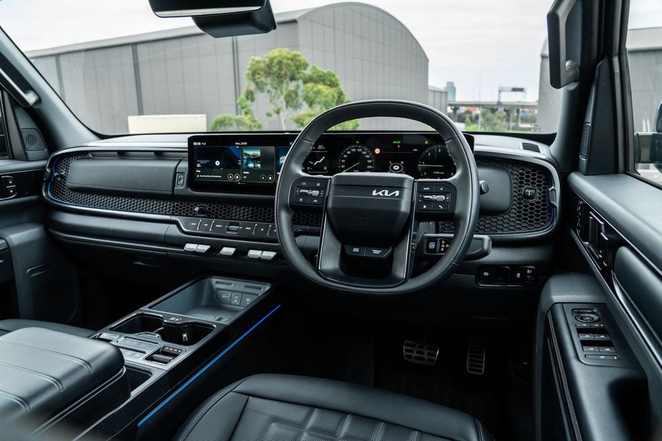 Interior of a Kia Tasman X-Pro showing the dashboard, steering wheel with Kia logo, dual digital screens, centre console and right-hand-drive layout