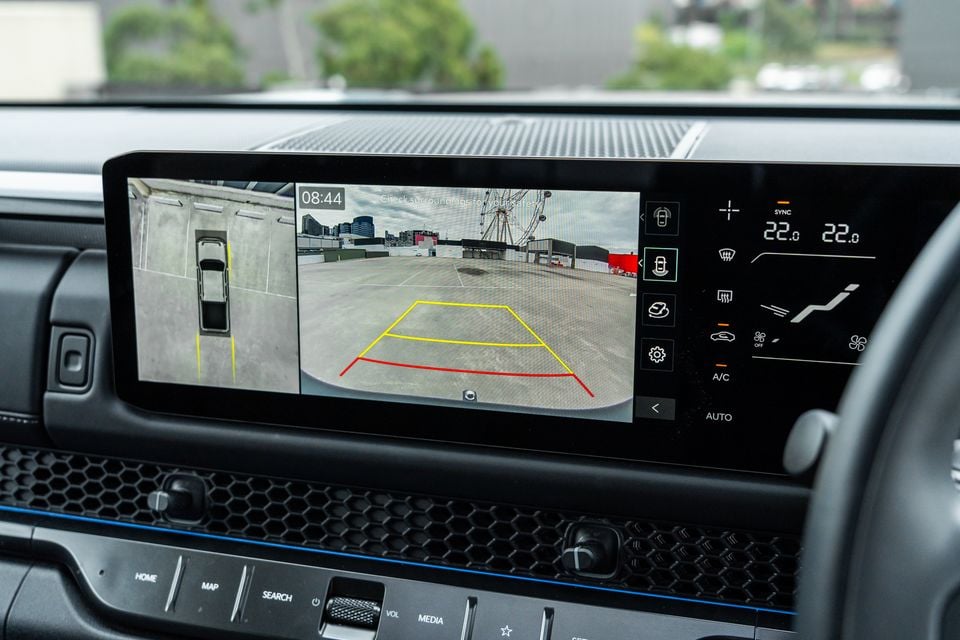 The infotainment screen of a Kia Tasman X-Pro displaying the reversing camera feed with parking guidelines, alongside a 360-degree surround view, and dual-zone climate controls to the right.