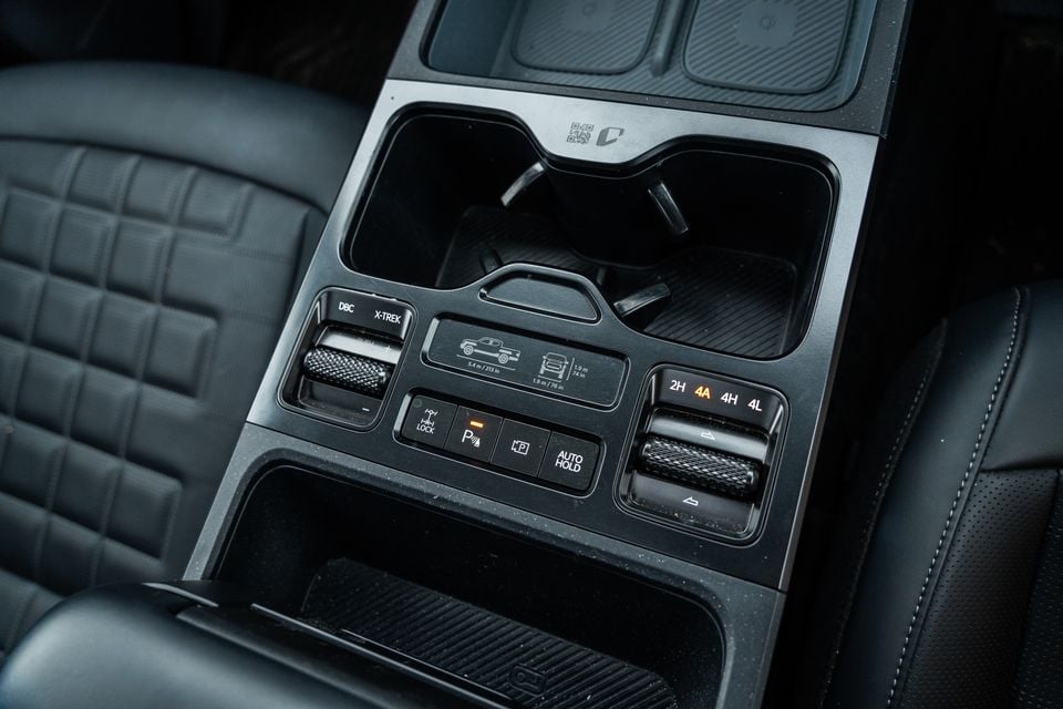 Close-up of the centre console controls in a Kia Tasman X-Pro, showing 4WD selector dial with 2H, 4A, 4H and 4L modes, DBC, X-Trek, Auto Hold, and hill descent buttons with black leather seats visible on either side