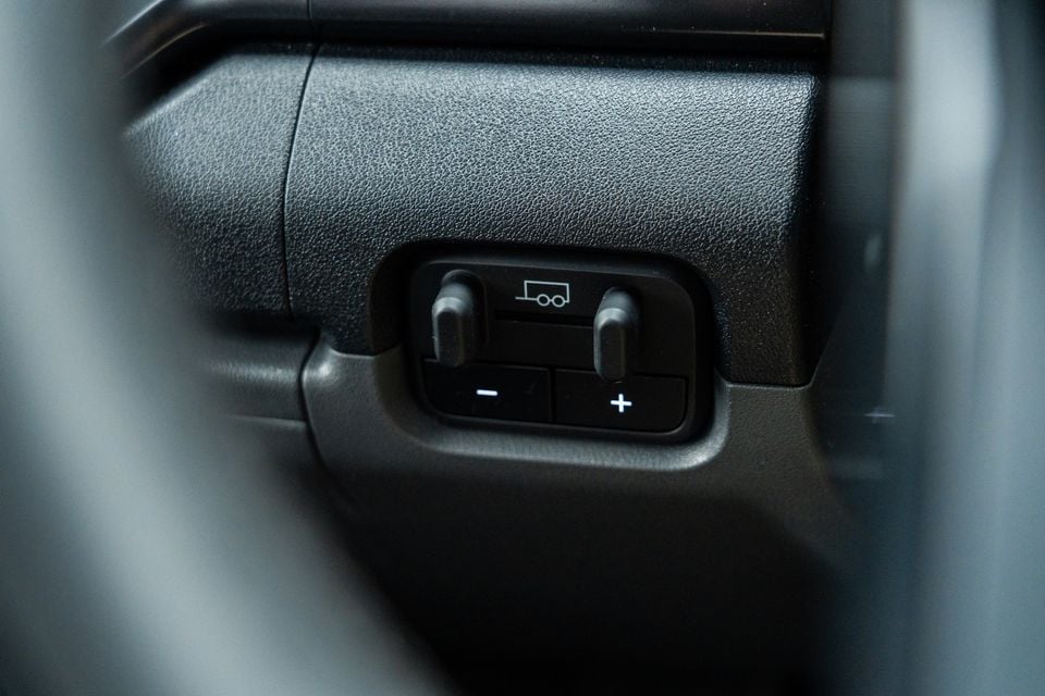 Close-up of a trailer brake controller panel with plus and minus buttons on the interior door trim of a Kia Tasman X-Pro