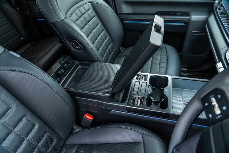 Interior view of the Kia Tasman X-Pro showing the centre console with cup holders, USB ports, controls, and quilted leather seats with blue ambient lighting