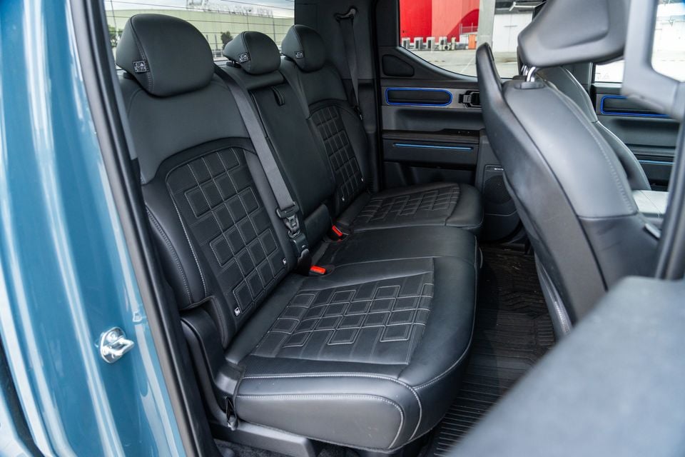 Rear seat interior of the Kia Tasman X-Pro showing black leather bench seating with quilted trim and blue accent lighting