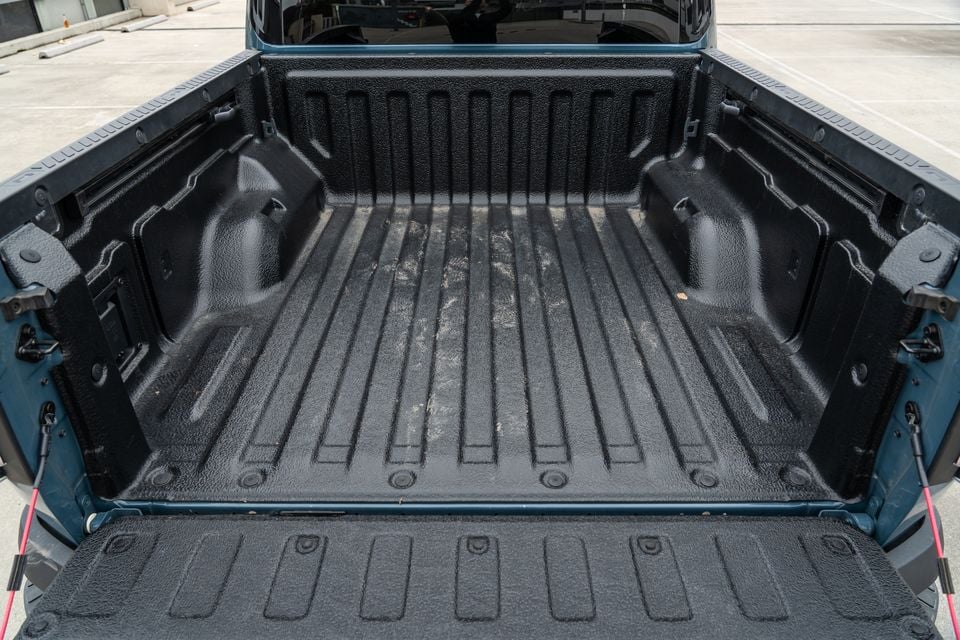 The open tub of a Kia Tasman ute showing a textured spray-on bed liner and lowered tailgate in a car park