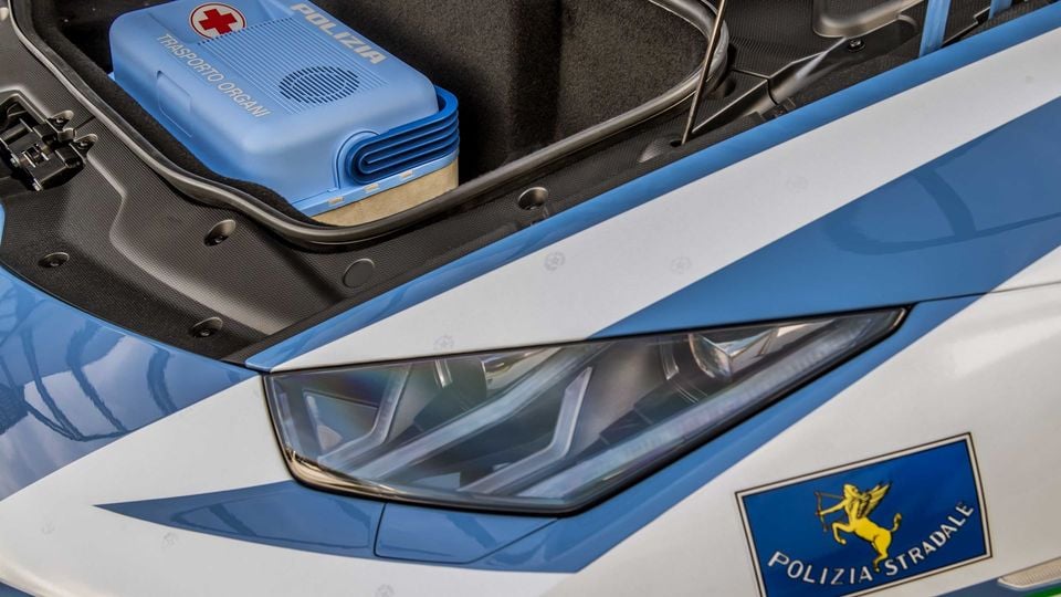 Close-up of a Lamborghini Huracan in Italian Polizia Stradale livery, showing the front headlight and open front trunk containing an organ transport case