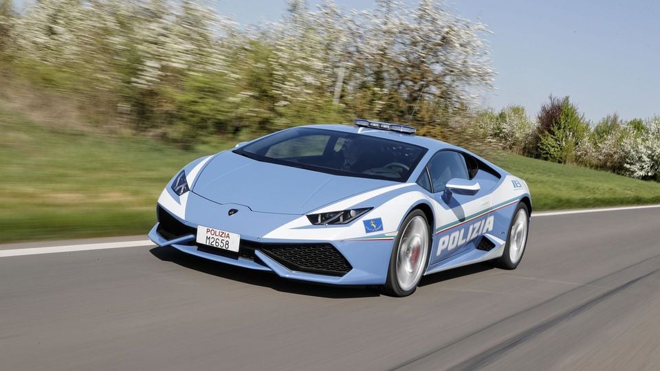 A Lamborghini Huracan in Italian Polizia livery driving on a road, seen from the front-side