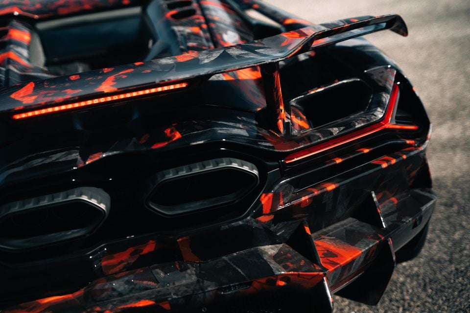 Close-up of the rear of a Lamborghini Revuelto SV prototype covered in a black and red camouflage wrap, showing quad exhausts, rear diffuser, and spoiler