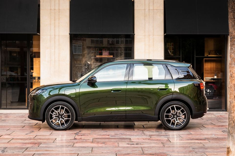 A dark green Leapmotor B03X small SUV seen in profile, parked on a paved street in front of shopfronts