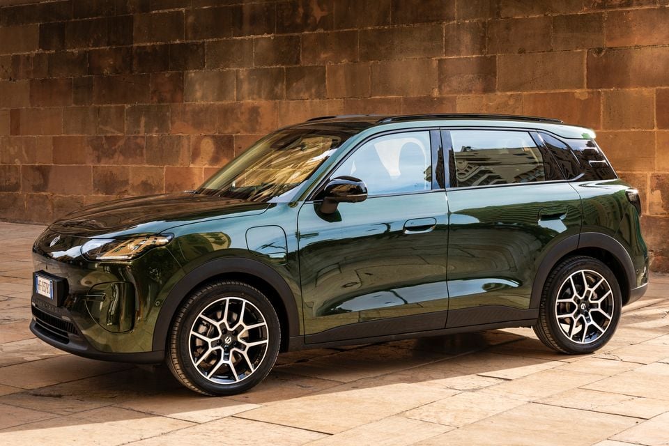 A dark green Leapmotor B03X small SUV with a black roof parked in front of a sandstone wall, seen from the front left side