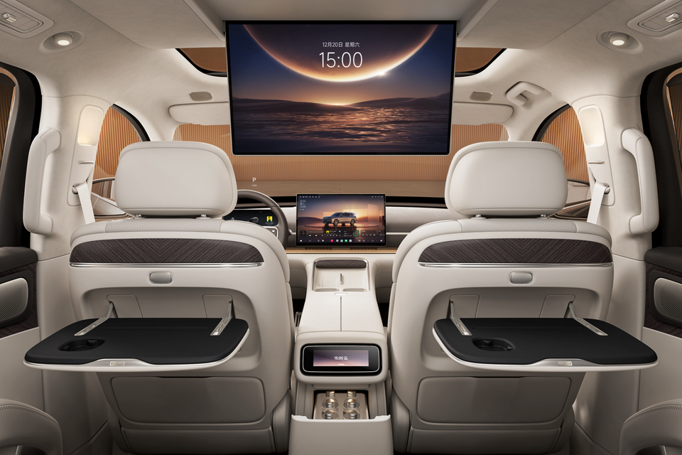 Leapmotor D19 cabin seen from the rear seats, with a large roof-mounted screen, fold-out tables on cream front seatbacks and a centre console fridge