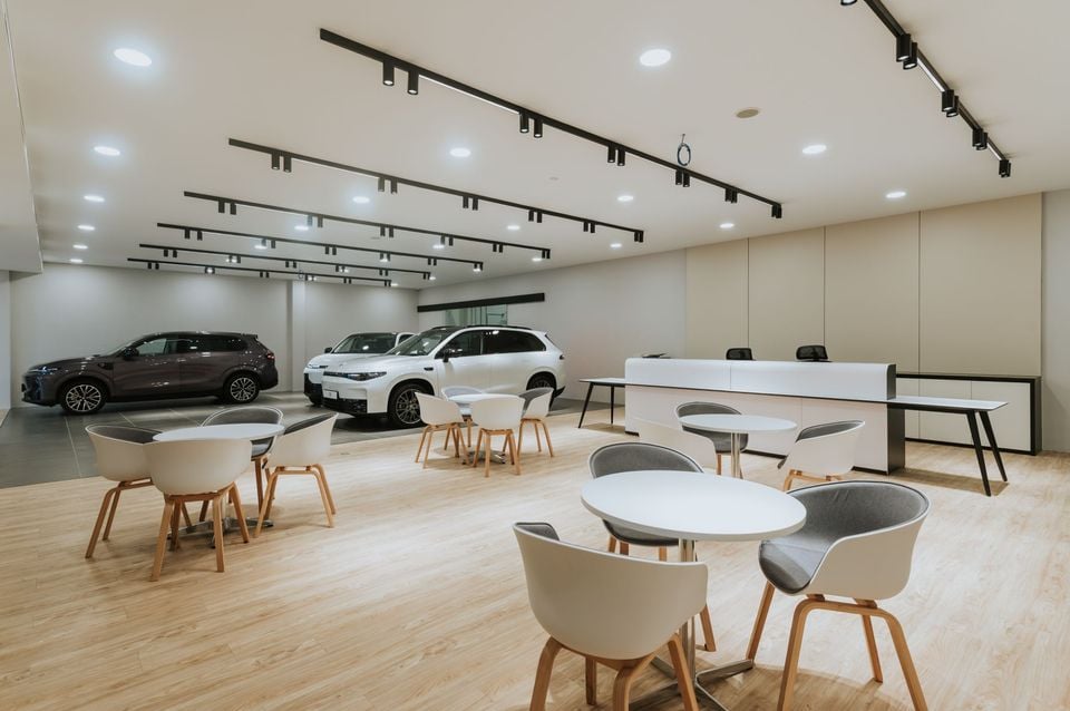 Interior of a modern Leapmotor car dealership showroom with SUVs on display, round white tables with chairs, a reception desk, and track lighting overhead.